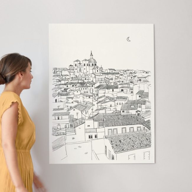 A lady standing next to an art print of a pencil drawing of Toledo